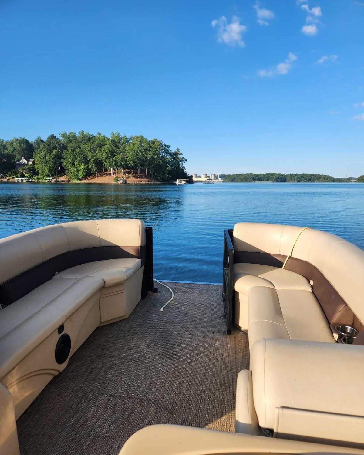 The view from the back deck of a tritoon, tan bench seats framing calm blue water and a wooded point on Lake Keowee.